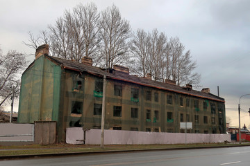 old three-story building, covered with a green grid for repairs on the street behind a gray fence