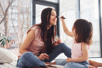 Learning how to make up. Young mother with her daughter spending weekend together in room