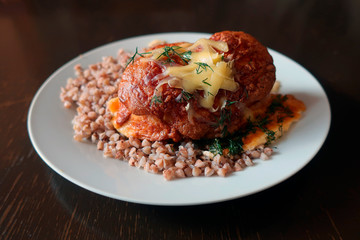 a piece of baked meat with cheese and buckwheat on a white plate