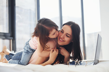 Young mother with her daughter spending weekend together in room and using laptop