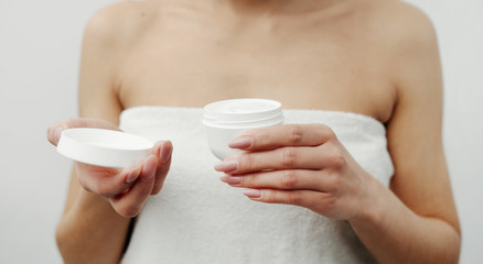 Impersonalized female in white bath towel holding open plastic cream jar, selective focus, isolated