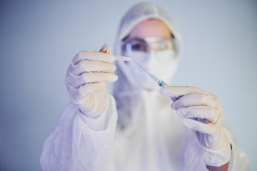 Holds syringe. Portrait of female doctor scientist in lab coat, defensive eyewear and mask