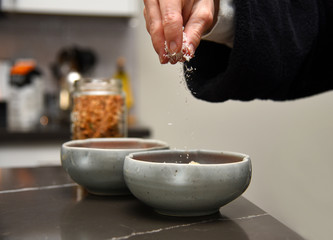 Obraz na płótnie Canvas Woman’s hand sprinkling coconut shavings into a ceramic bowl while making a granola smoothie