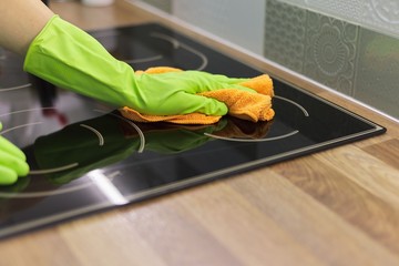 Woman hand in gloves polishing hob glass with microfiber cloth