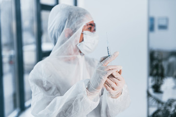 Holds syringe. Portrait of female doctor scientist in lab coat, defensive eyewear and mask
