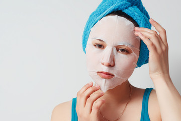 a young beautiful woman uses a fabric cosmetic face mask with a towel wrapped around her head.