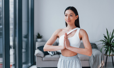 Fototapeta na wymiar Does yoga exercises. Young woman with slim body shape in sportswear have fitness day indoors at home