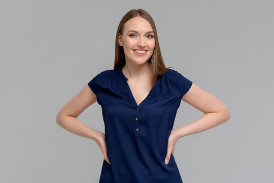 Beautiful Smiling Young Woman With Braces In Dress Is Holding Hands On Hip And Looking At Camera. Three Quarter Length Studio Shot On Monochromatic Background.