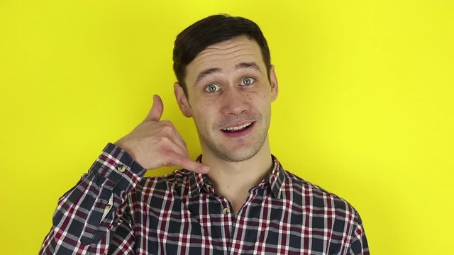 A funny, cute guy asks for a callback and makes a hand gesture. Portrait of a young guy, he makes a hand gesture next to his ear asking for a callback. Portrait on a yellow background.