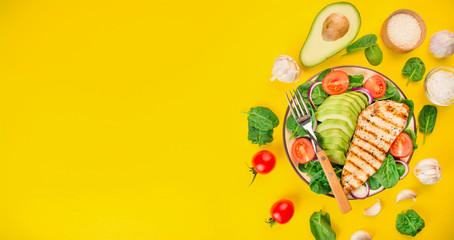 Grilled chicken breast and fresh vegetable salad with spinach leaves, avocado and tomatoes on a yellow background. Healthy food. Dietary nutrition. View from above. Copy space. Banner.