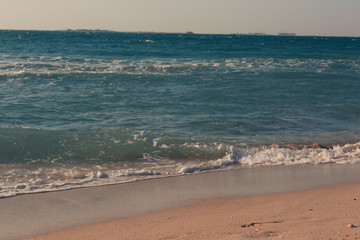 Tropical beach white sand, blue clear ocean water. sea foam on the beach on a sunny day. sea waves on the shore. surf breaking on shore at sunset