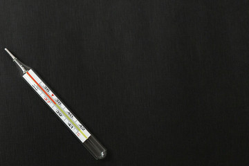 thermometer with high temperature on a black background, coronavirus top view