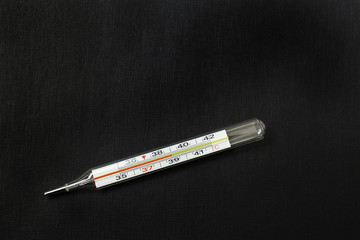 thermometer with high temperature on a black background, coronavirus top view