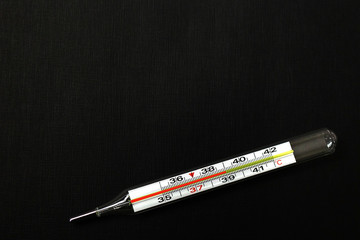thermometer with high temperature on a black background, coronavirus top view