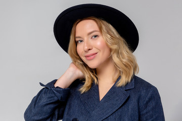 Fashionable woman in blue coat and black hat posing in studio, looking at camera. cold season. Autumn, Spring or winter look.