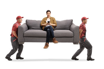 Movers carrying a sofa with a young man sitting and using a mobile phone