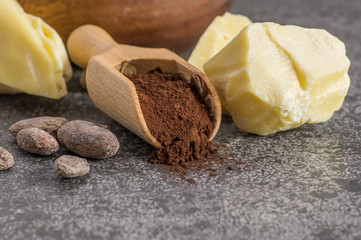 Cocoa butter or Cocoa bean solid oil with cacao powder in spoon and raw cocoa beans on rustic backdrop, healthy natural oil