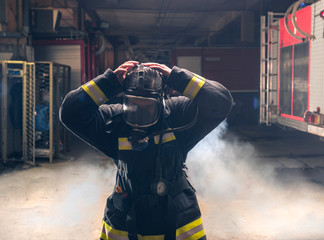 Portrait of a fireman wearing firefighter turnouts putting on oxygen mask. Dark background with smoke and blue light.