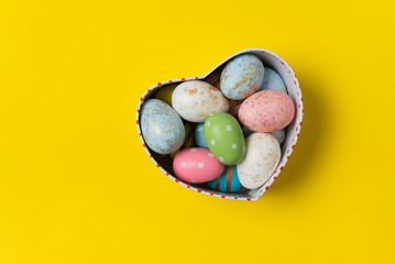 Heart shaped box with colorful Easter eggs on bright yellow background. Holiday eggs