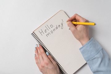 Hello monday text in copybook. Female hands writing note in Notepad. White background