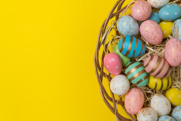 Closeup of Easter eggs in basket on yellow background. Top view of festive eggs