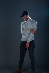 Male model with a black hat posing in a studio wearing white blouse and black pants