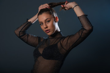 Fashion portrait of an attractive brunette girl holding and pulling her ponytail.