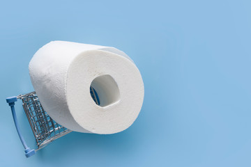 Grocery trolley with roll of soft toilet paper on blue table with space for text. Covid-19 pandemic. Increased potential. High unexpected demand. Deficit.