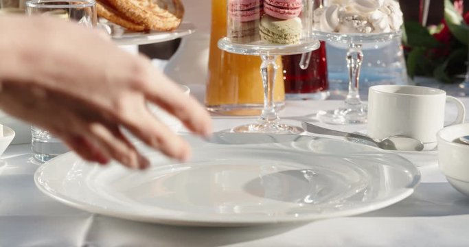 Close up shot of hands of a waiter preparing dishes for client's breakfast at hotel, putting a plate, napkin, fork and knife on table with snacks 4k footage