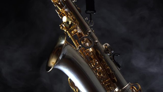 Golden shiny alto saxophone slowly move on black background with smoke