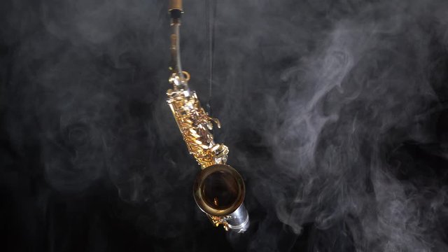 Golden shiny alto saxophone slowly move on black background with smoke