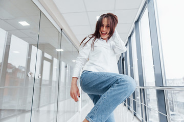 Close up view of brunette in white shirt indoors in modern airport or hallway at daytime that making kick with leg