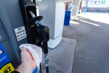 A mans hand with a disinfecting wipe in it holding a gas pump as a precaution during the...