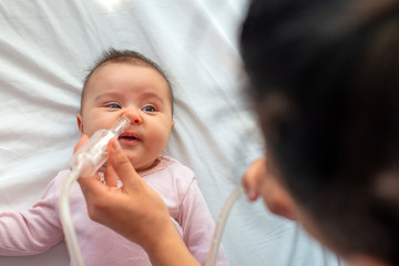 Close up of caring  mother with nasal pump to clean her baby's nose. Baby lying in bed