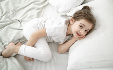 A cute little girl is sleeping in a white bed .