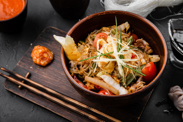 Chinese dishes in a clay plate on a black concrete background with ingredients for delivery