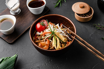 Chinese dishes in a clay plate on a black concrete background with ingredients for delivery
