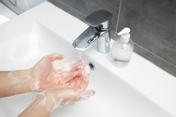 A man washes his hands with antibacterial soap under a tap with water. Treats hands with an antiseptic during the coronavirus pandemic