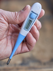Male hand holds clinical thermometer with quarantine text on the screen during global covid-19 or corona pandemic