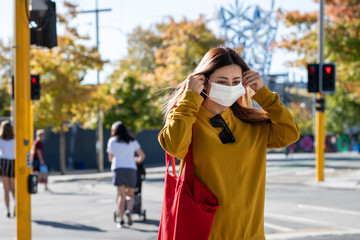 A beautiful middle aged Asian woman wearing a medical mask to protect from infection of virus, pandemic, outbreak and epidemic of disease in Christchurch city, New Zealand. Social distancing. 