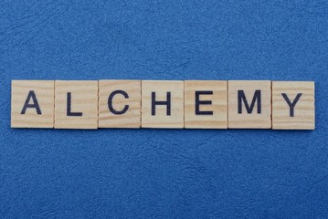 word alchemy from small gray wooden letters lies on a blue background