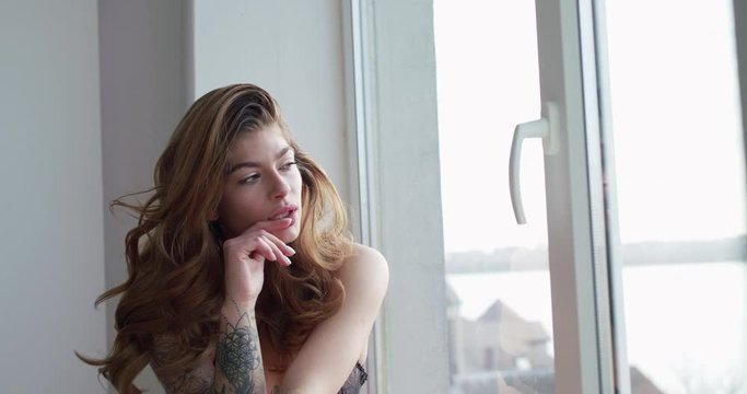 Elegant woman in underwear poses with hair and thinks on windowsill