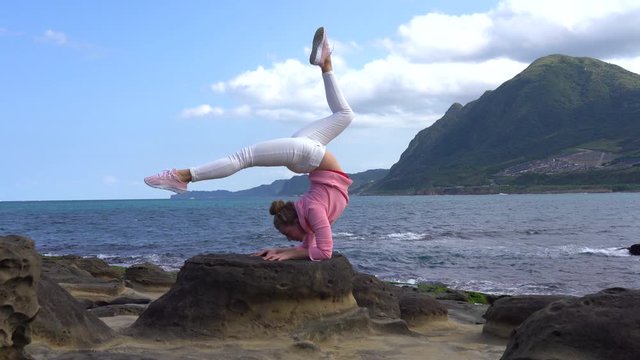 Beautiful girl on the volcanic shore in bright casual clothes on a sunny day in 4K. yoga outside on background of green mountains. Flexible girl doing acroyoga on the ocean in Taiwan. Elephant rock