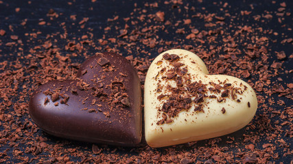 Two heart-shaped chocolates made of milk and white chocolate on the slate board, covered in grated chocolate. Desserts for Valentine's Day.