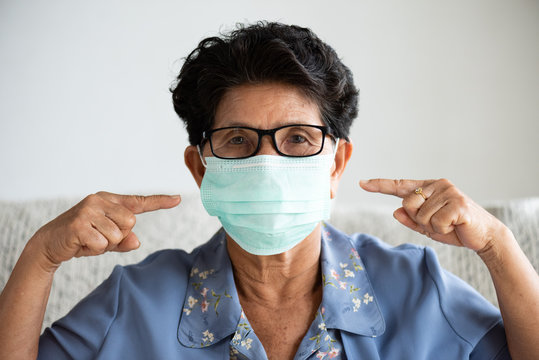 Sick Asian Old Woman Wearing Protective Face Mask, Get Ready For Coronavirus And Pm 2.5 Fighting, Sitting On Sofa At Home. Senior Healthcare Concept.