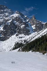 Two people walking on frozen mountain lake. 