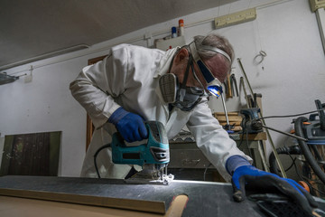 specialist worker cutting carbon part with goggles, gloves and dust protection, for race car in workshop.
