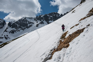A lonely hiker in the mountains heading snow-capped peaks in the early spring