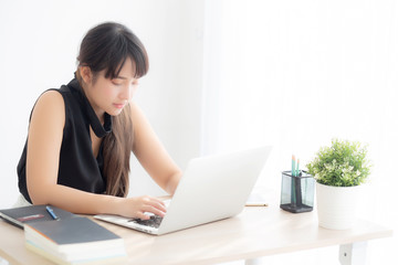 Fototapeta premium Beautiful freelance asian woman smiling working and typing on laptop computer at desk office with professional, girl using notebook checking email or social network, business and lifestyle concept.