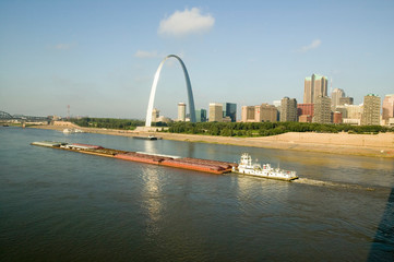 Daytime view of tug boat pushing barge down Mississippi  River in front of Gateway Arch and skyline of St. Louis, Missouri as seen from East St. Louis, Illinois on the Mississippi River - obrazy, fototapety, plakaty